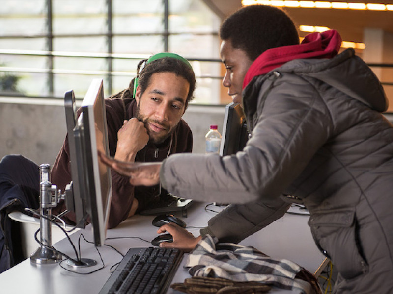 Een vrouw wijst iets aan op een computerscherm waar een man naar kijkt