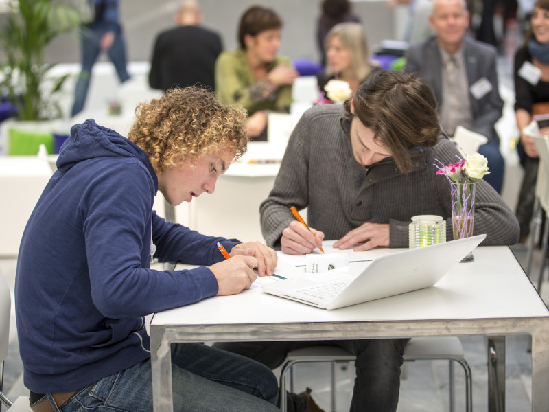 Twee studenten schrijvend aan een tafel met laptop