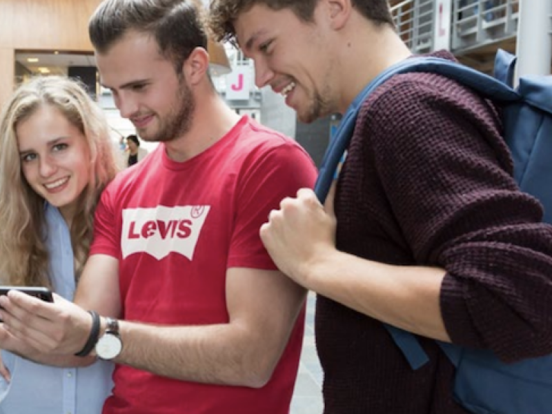 Vier studenten kijkend naar een mobiele telefoon