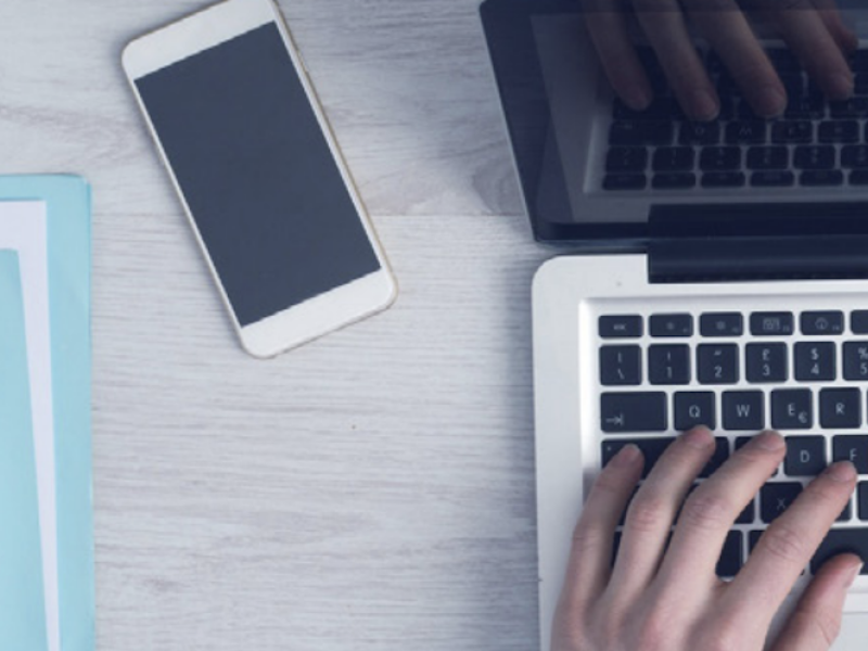 Man aan laptop met mobiel van bovenaf gefotografeerd