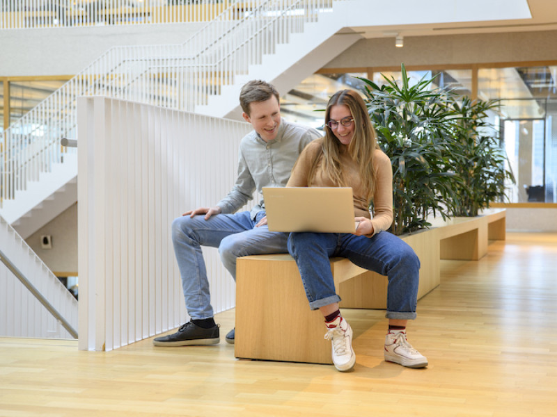 Twee studenten in een open hal met een laptop