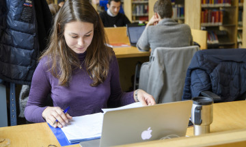 Studente in bibliotheek met laptop en papierwerk 
