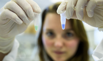 Onderzoeker die twee buisjes met gekleurde vloeistof omhoog houdt in lab 