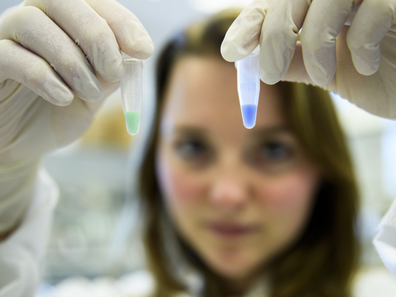 Onderzoeker die twee buisjes met gekleurde vloeistof omhoog houdt in lab 