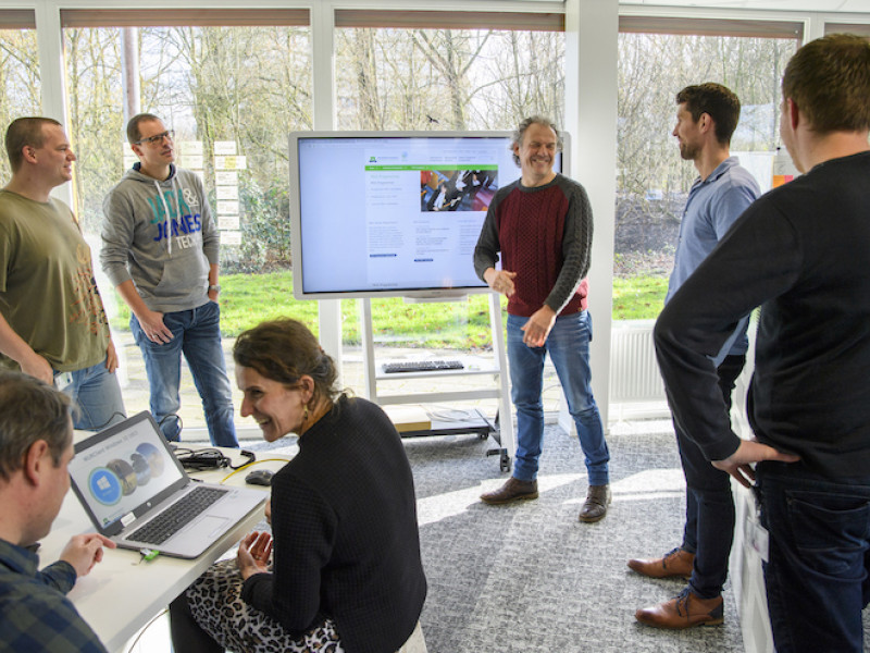 Groep mensen staand voor een groot scherm met elkaar in overleg