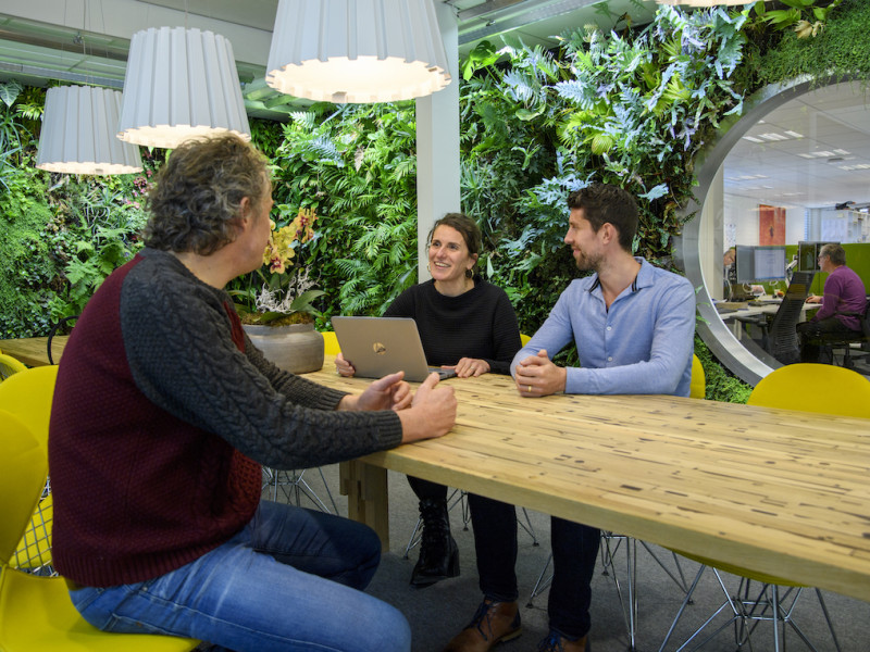 Drie mensen met computer aan het een tafel in gesprek