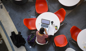 Studente achter laptop aan tafel met rode stoelen van bovenaf gefotografeerd