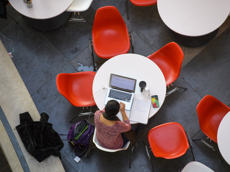 Studente achter laptop aan tafel met rode stoelen van bovenaf gefotografeerd