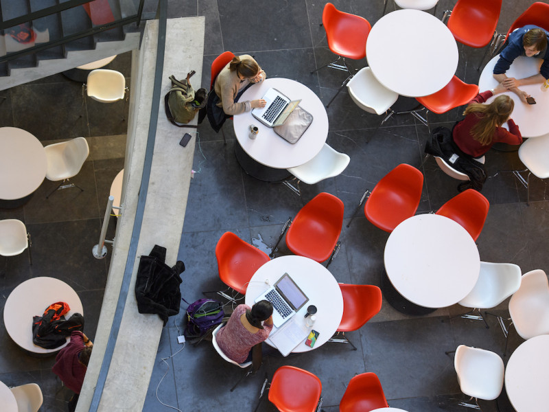 Studenten individueel aan tafels in open ruimte met verschillende devices