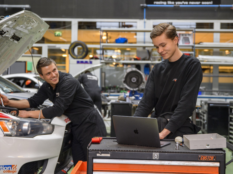 Twee jonge monteurs met elektrische auto en laptop