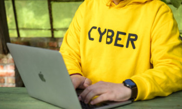 Man in gele trui met CYBER erop achter de laptop