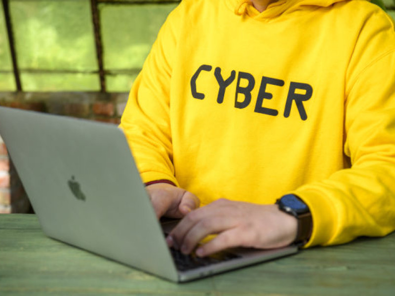 Man in yellow jersey with CYBER on it behind laptop