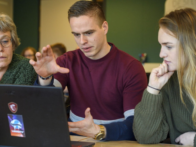 Twee jonge onderzoekers met een oudere dame samen achter een laptop