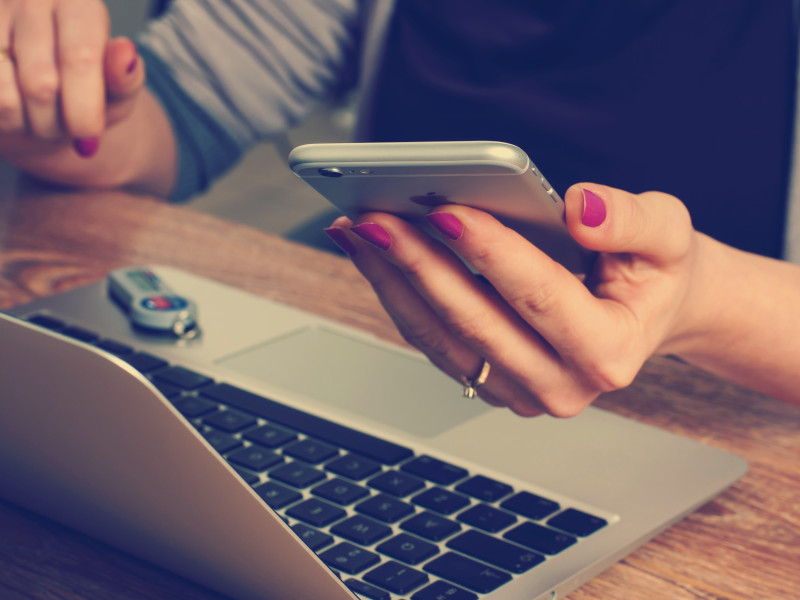 Foto van een vrouw die een mobiele telefoon vasthoudt en achter haar laptop zit.