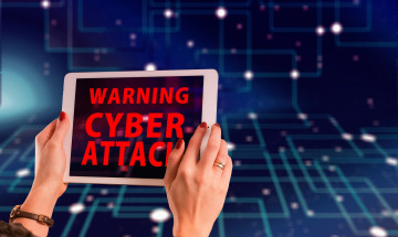 Een vrouw houdteen tablet vast met daarop de tekst 'Warning cyber attack' 