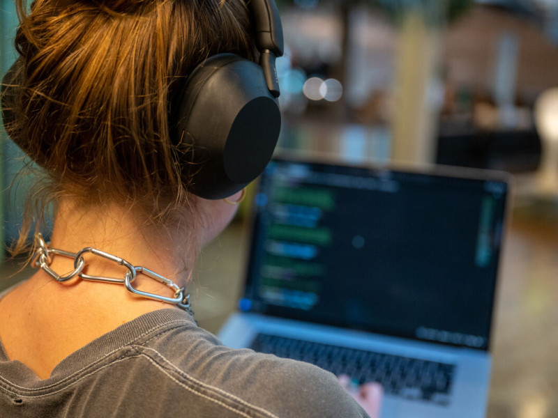 Vrouw met koptelefoon gefotografeerd op haar achterhoofd kijkt naar laptop waarvan het scherm onscherp is