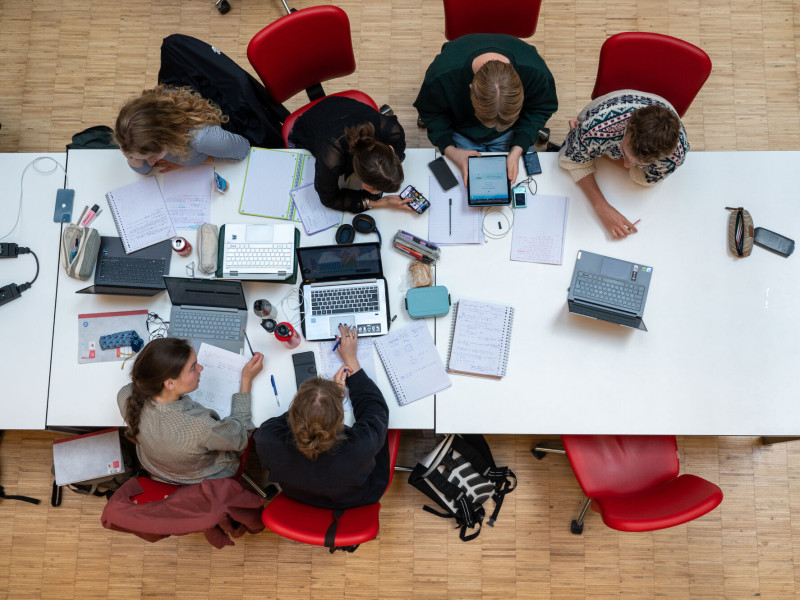 Bovenaanzicht van 6 studenten die samen studeren aan een lange tafel