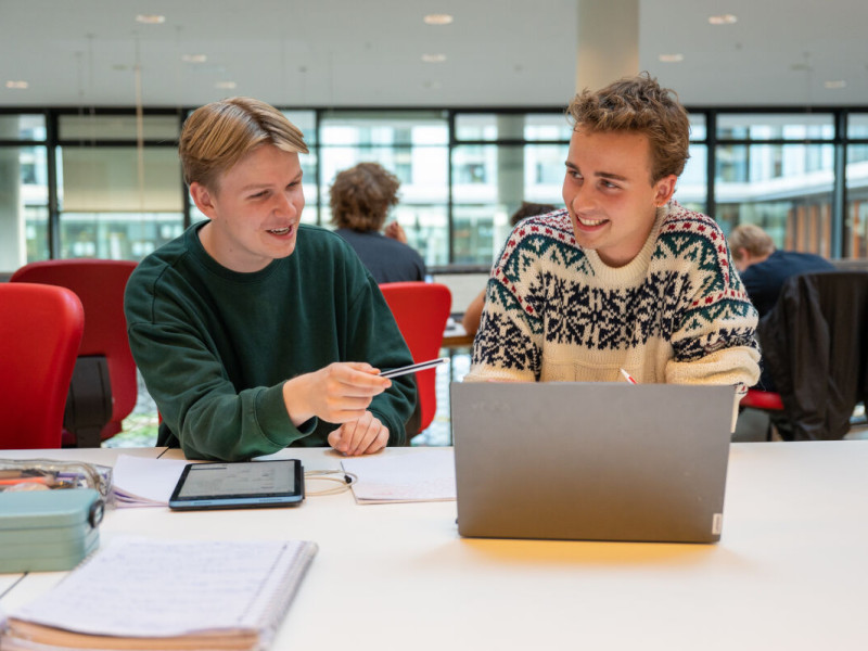 Twee studenten werken op een laptop, de linker wijst naar het scherm