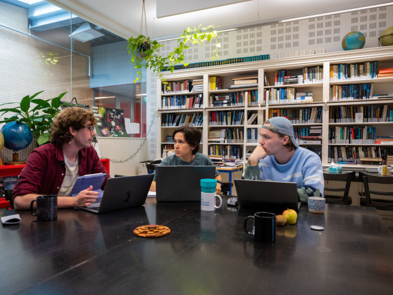 drie studenten in gesprek aan tafel achter hun laptop