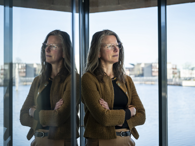 Nolda staat voor een raam met water op de achtergrond en kijkt in de verte