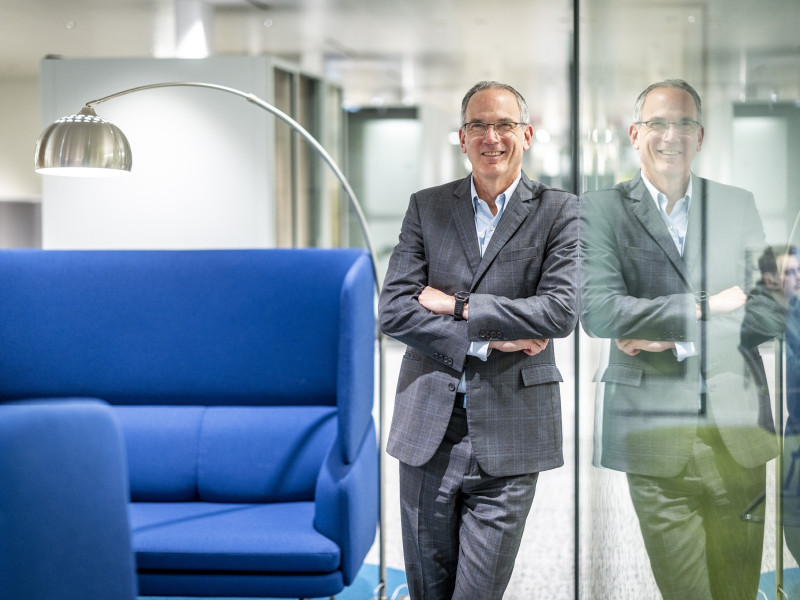 Paul Hillman staat in de gang en leunt tegen een glazen wand