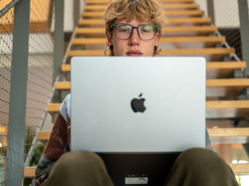 student zit op de trap en werkt op zijn apple laptop
