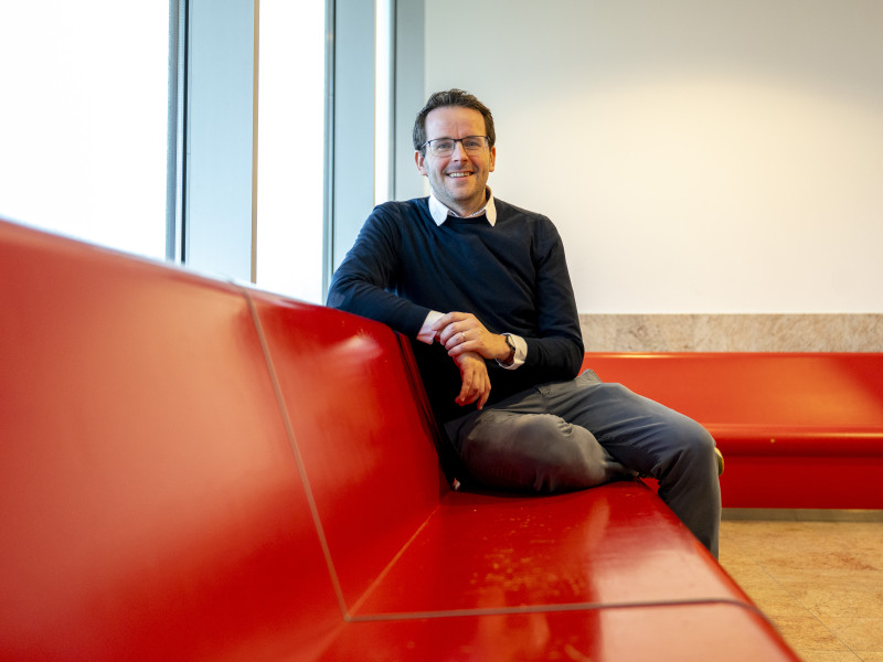 Tom Emery zit en kijkt lachend de camera in