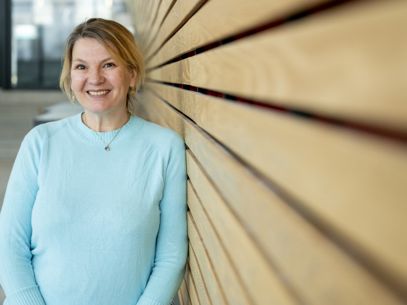 Eveline Crone leunt tegen muur en kijk lachend naar de camera