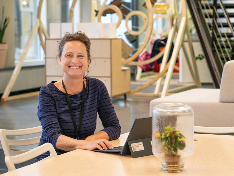 Astrid van Wesenbeeck zit aan tafel met haar laptop en kijk lachend naar de camera