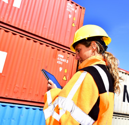 Vrouw in beschermende kleding met tablet bij zeecontainers