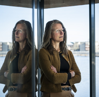 Nolda staat voor een raam met water op de achtergrond en kijkt in de verte
