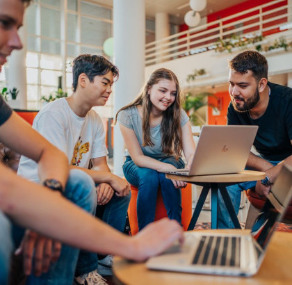 Studenten achter laptops aan lage tafels in een open ruimte in een instelling