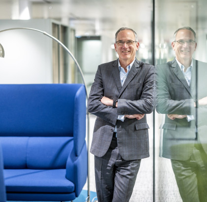 Paul Hillman staat in de gang en leunt tegen een glazen wand