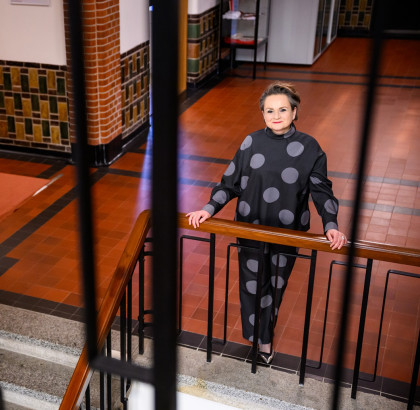 Alexandra van Huffelen stands next to a staircase and looks into the camera, smiling. 