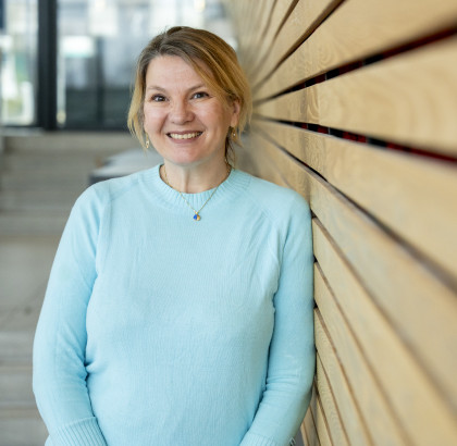 Eveline Crone leunt tegen muur en kijk lachend naar de camera